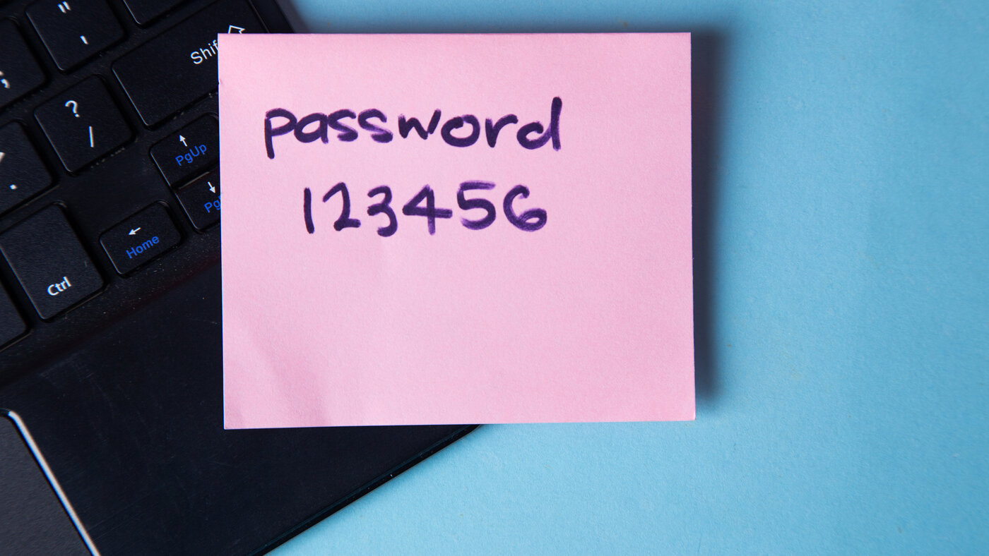 A pink sticky note handwritten with the word password and the digits 123456, stuck to a black laptop keyboard against a blue background